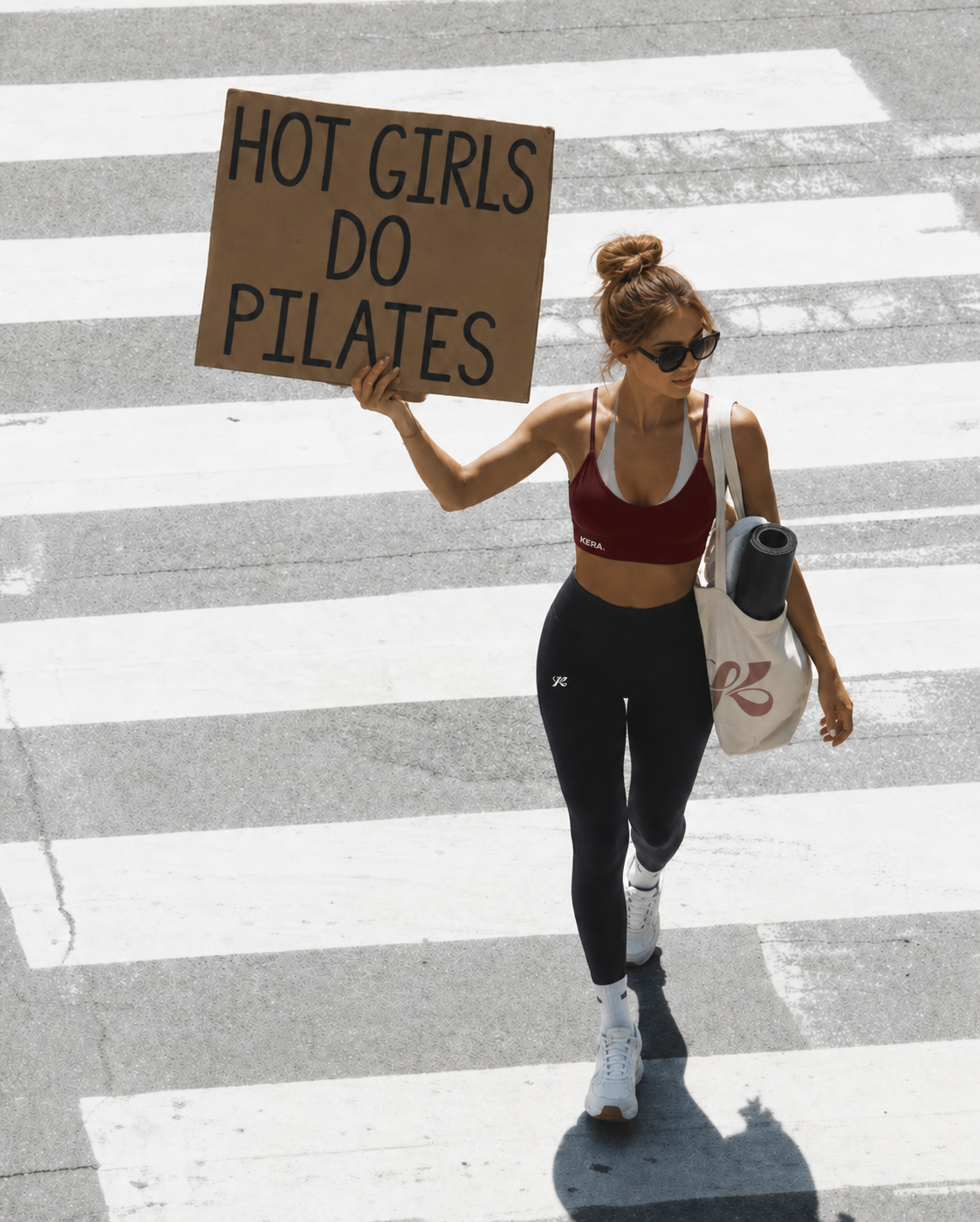 Femme en tenue KERA traversant la rue avec une pancarte « Hot Girls Do Pilates »
